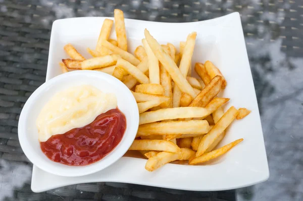 Вкусная картошка фри в белых тарелках на стеклянном фоне стола — стоковое фото