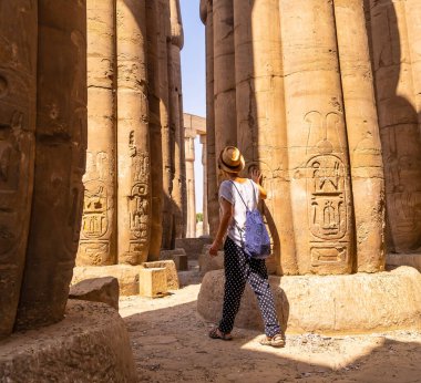 Beyaz tişörtlü ve şapkalı genç bir turist, Mısır 'daki Luxor Tapınağı sütunlarındaki antik Mısır çizimlerine bakıyor.