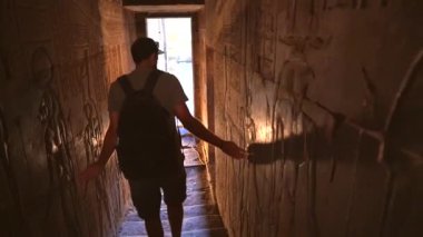 Genç bir adam Aswan yakınlarındaki Edfu Tapınağı 'nın tünellerini ziyaret ediyor. Mısır. Arkadan takip eden uçak. Edfu şehrindeki Nil Nehri, Greko-Romen inşaatı, Horus 'a adanmıştır.