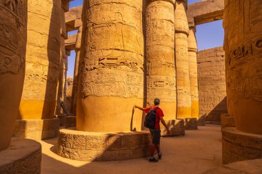 Amun 'un büyük mabedi Karnak Tapınağı' nın içinde hiyerogliflerle sütunların arasında yürüyen genç bir turist. Mısır