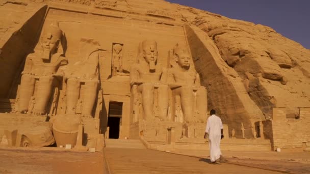ヌビアのナセル湖の隣にあるエジプト南部のアブ シンベルの神殿に向かって歩いている地元の男 ファラオラムセス2世の神殿 4Kビデオ — ストック動画