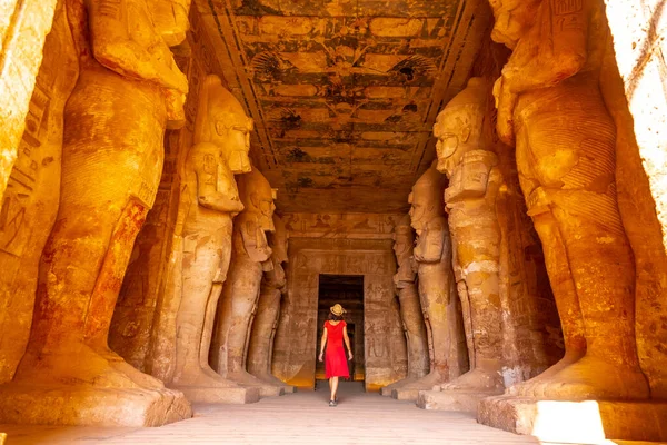 位于埃及南部努比亚靠近纳赛尔湖的阿布辛贝尔神殿 一位身穿红色连衣裙的年轻女子在雕塑旁边 法老的庙宇拉姆西斯二世 旅行生活方式 — 图库照片