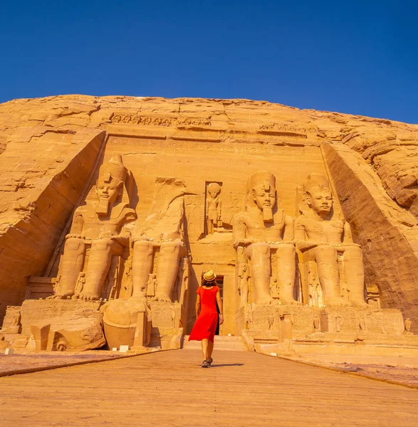 ヌビアのナセル湖の隣にあるエジプト南部のアブ シンベル寺院に向かって歩いている赤いドレスを着たヨーロッパの観光客 ファラオラムセス2世の寺院 旅行生活 — ストック写真