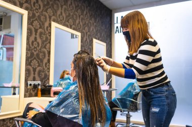 Maskeli bir kuaför, boyayı müşterinin gri saçına maskeyle uyguluyor. Covid-19 salgınında kuaförlerin güvenlik önlemleriyle yeniden açılması, Coronavirus