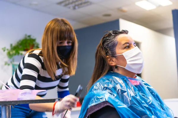 Detail of Hairdresser with mask applying the dye to the client with mask. Reopening with security measures of Hairdressers in the Covid-19 pandemic, coronavirus