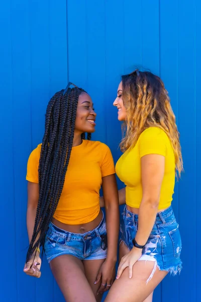 年轻的女朋友们穿着黄色的T恤 穿着蓝色的墙背景的衣服 彼此反映出彼此的爱 留着长长的辫子 金发白妞 — 图库照片