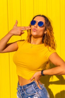 Yaşam tarzı, sarı gömlekli, sarı arkaplanlı beyaz sarışın kız. Sokak ve şehir ifadeleriyle poz veren, güneş gözlüğü takan şık güzel bir kız.