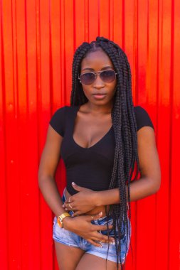 Yaşam tarzı, siyah tişörtlü siyah kız, kot şort ve kırmızı arka planda güneş gözlüğü. Yaz öğleden sonranın tadını çıkarıyorum.