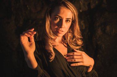 Yaşam tarzı, siyah elbiseli, mağaradaki fotoğrafta sarı ışıkla aydınlatılmış beyaz bir sarışın. Sonbahar öğleden sonra eğlenen genç kadının portresi.