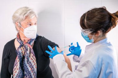 Yaşlı bir kadın bir doktor tarafından koronavirüs aşısı yaptırılıyor. Antikorlar, nüfusu aşılayın. yan etkiler, risk insanları, antikorlar, yeni normal, covid-19.