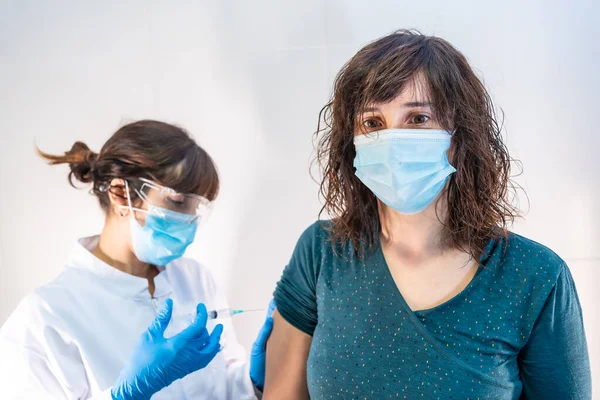 A woman doctor with a face mask applying the coronavirus vaccine to a young woman at risk. First vaccines for people at risk, antibodies, new normal, covid-19.