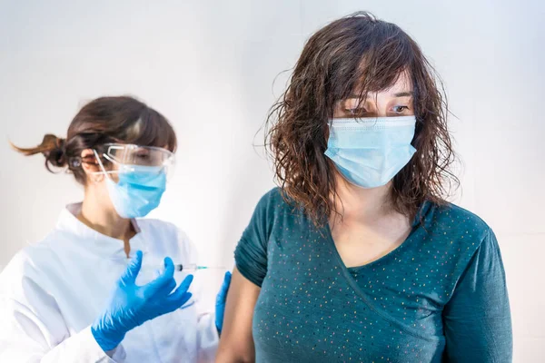 A female doctor with a face mask applying the coronavirus vaccine to a young patient. First vaccines for people at risk, antibodies, new normal, covid-19.