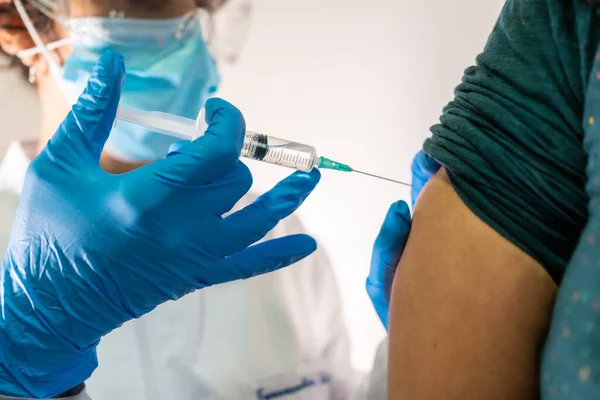 Female doctor with face mask applying the coronavirus vaccine, detail of the infection. Side effects, risk people, antibodies, new normal, covid-19.