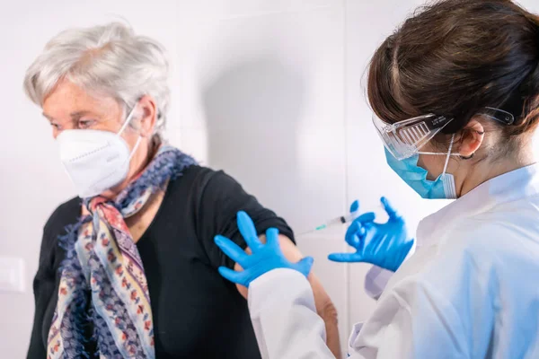 Yaşlı bir kadın koronavirüs aşısı yaptırıyor. Antikorları alması ve halkı bağışık hale getirmesi için bir doktor tarafından. yan etkiler, risk insanları, antikorlar, yeni normal, covid-19.