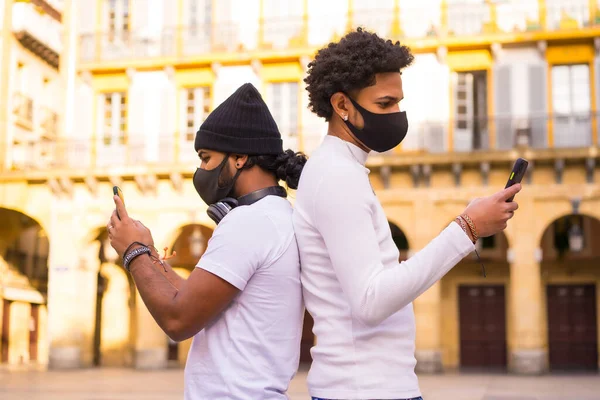 ライフスタイル 黒いラテン系の友人マスクで携帯電話にメッセージを書く コロナウイルスのパンデミックにおける友情 Covid 社会的距離 新常態 — ストック写真