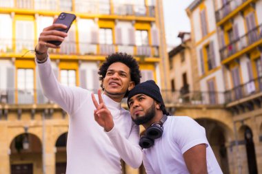 Yaşam tarzı, iki siyah Latin arkadaşın sokakta selfie çekmesi. Afro saçlı çocuk ve şapka ve kulaklıklı çocuk.