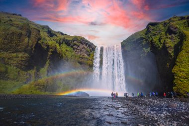 Güney İzlanda 'daki etkileyici Skogarfoss şelalesine bakan bir grup turist, yazın güzel bir gün batımında çekilmiş bir fotoğraf.