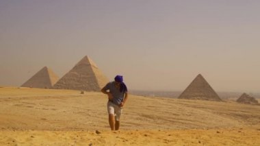 Mavi elbiseli genç bir turist ve Giza piramitlerinin yanında yürüyen bir türbanlı. Kahire, Mısır