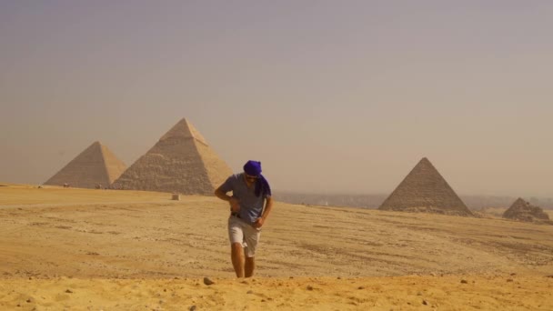 一个身穿蓝色衣服头戴头巾的年轻游客走在吉萨金字塔旁边 埃及开罗 — 图库视频影像