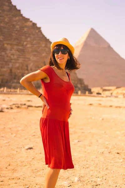 Portrait of a young pregnant woman in red dress at the pyramid of Cheops the largest pyramid. The pyramids of Giza the oldest funerary monument in the world. In the city of Cairo, Egypt