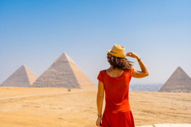 Kırmızı elbiseli genç bir turist dünyanın en eski Cenaze Anıtı Giza Piramitlerine bakıyor. Mısır 'ın Kahire şehrinde
