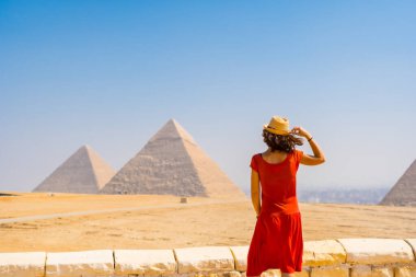 Kırmızı elbiseli genç bir turist dünyanın en eski Cenaze Anıtı Giza Piramitlerine bakıyor. Mısır 'ın Kahire şehrinde