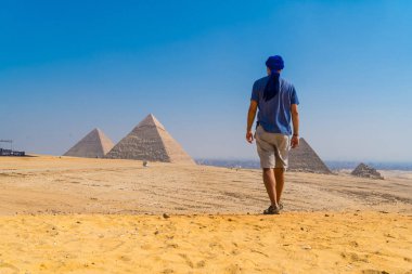 Dünyanın en eski cenaze anıtı olan Giza Piramitleri 'nin yanında yürüyen mavi sarıklı genç bir adam. Mısır 'ın Kahire şehrinde
