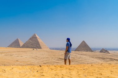 Dünyanın en eski cenaze anıtı olan Giza Piramitleri 'nin yanında yürüyen mavi sarıklı genç bir adam. Mısır 'ın Kahire şehrinde