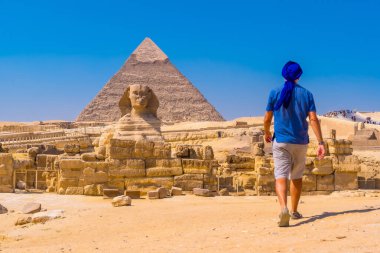 Giza 'nın Büyük Sfenksi' ne doğru yürüyen genç bir adam ve arka planda Giza piramidi Khafre 'nin piramidi. Kahire, Mısır