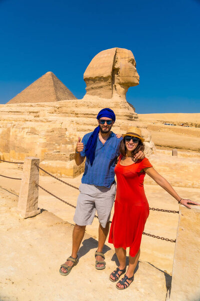 A tourist couple at The Great Sphinx of Giza and in the background the Pyramids of Giza, the oldest Funerary monument in the world. In the city of Cairo, Egypt