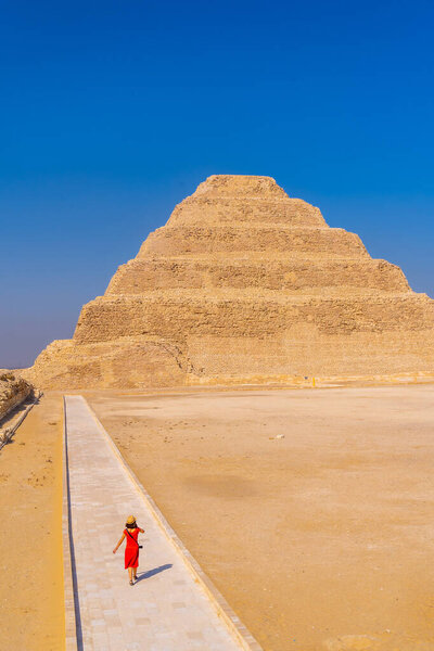 A young woman in a red dress visiting the Stepped Pyramid of Djoser, Saqqara. Egypt. The most important necropolis in Memphis. The first pyramid in the world