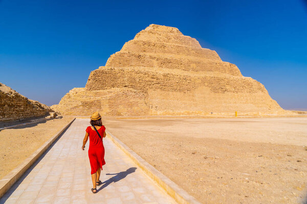 A young tourist in a red dress at the Stepped Pyramid of Djoser, Saqqara. Egypt. The most important necropolis in Memphis. The first pyramid in the world