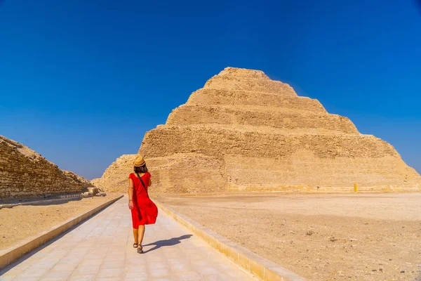 Saqara 'daki Djoser Piramidi' nde kırmızı elbiseli genç bir turist. Mısır. Memphis 'teki en önemli mezarlık. Dünyanın ilk piramidi.