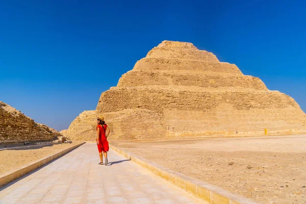 一名身穿红色礼服的年轻游客在萨卡拉的Djoser的阶梯金字塔 孟菲斯最重要的墓地世界上第一个金字塔 — 图库照片