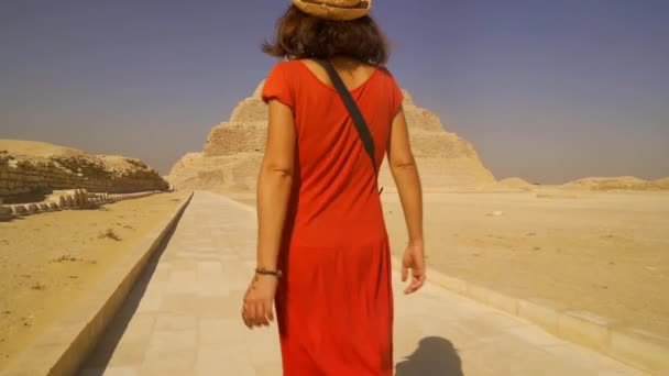 在萨卡拉的Djoser的台阶金字塔 一名身穿红色衣服的年轻旅游女孩走在台阶上 孟菲斯最重要的墓地世界上第一个金字塔 — 图库视频影像