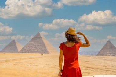 Kırmızı elbiseli genç bir turist dünyanın en eski Cenaze Anıtı Giza Piramitlerine bakıyor. Mısır 'ın Kahire şehrinde