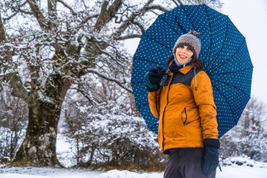 Dev bir karlı ağacın yanında sarı ceketli ve şemsiyeli genç bir kızın portresi. Araba, Bask ülkesinin Vitoria yakınlarındaki Opakua kasabasında kar. İspanya