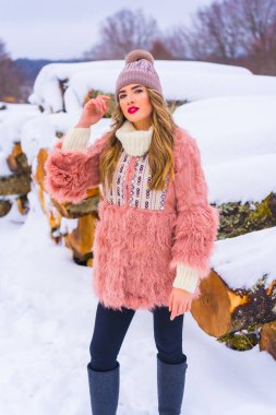 Pembe kürk ceketli ve karda mor şapkalı sarışın bir manken. Buzdan kesilen bazı ağaçların yanında, kış yaşam tarzı.