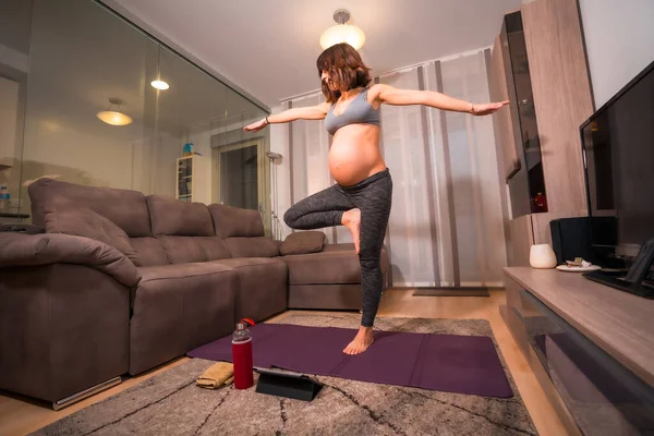 若い妊婦の白人女性が自宅のリビングルームでピラティス運動をしています 授業前のオンライン演習 — ストック写真