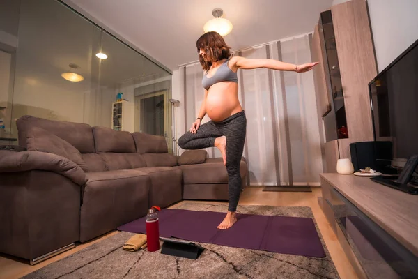 グレーのTシャツを着た若い妊婦の白人女性が自宅でピラティスの練習をしています 授業前のオンライン演習 — ストック写真