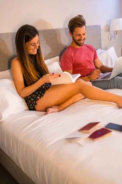 一对英俊的白人夫妇躺在旅馆的床上 看着一台电脑和一本书 夏季生活方式 — 图库照片
