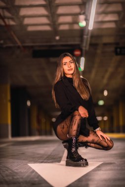 Siyah ceketli, beyaz okun üzerinde, boş bir otoparkta beyaz bir esmer. Şehirde gece şehir toplantısı.