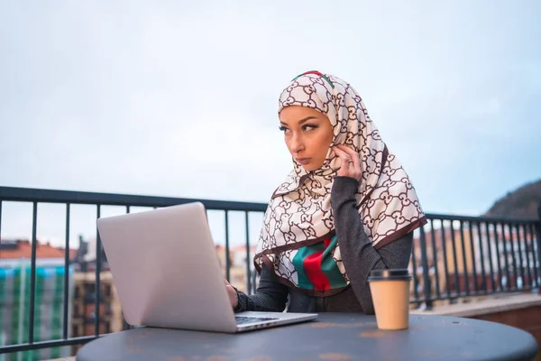 阿拉伯女孩披着白色的面纱 坐在一家咖啡店的阳台上 苦思冥想地做着一件事 拥有新技术的现代阿拉伯年轻人 — 图库照片