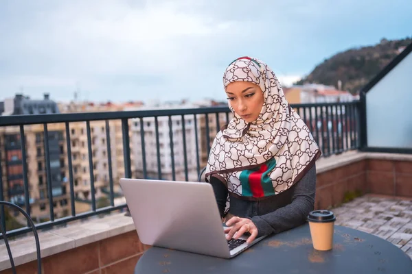 一个阿拉伯女孩 拿着白色的面纱在电脑前的一个长颈鹿店的阳台上工作 拥有新技术的现代阿拉伯年轻人 — 图库照片