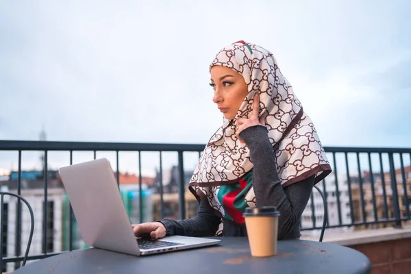 一个阿拉伯女孩带着一个白色的面纱在电脑前的一个长颈鹿店的阳台上 与电脑形成反差 拥有新技术的现代阿拉伯年轻人 — 图库照片