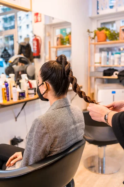 Hairdresser with a mask giving the final touches to the brunette client\'s hairstyle. Security measures of Hairdressers in the Covid-19 pandemic