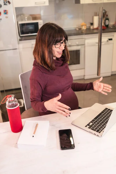由于工作困难 年轻的孕妇在家用电脑远程工作 一边打电话一边笑着 — 图库照片