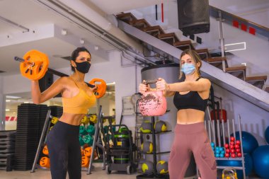 Spor salonlarında koronavirüs salgını. Yüz maskeli, sosyal mesafeli ve yeni normal kilolu kızlar.