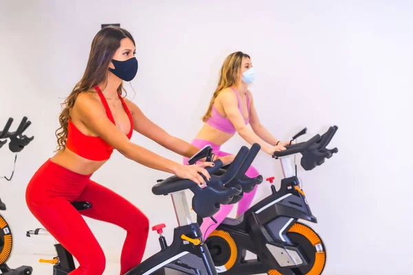 Coronavirus pandemic in gyms. Two girls training on bikes with face masks, social distance and a new normal