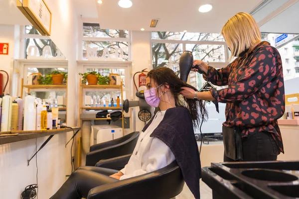 Hairdresser with face protection mask drying the client\'s hair with a hairdryer. Security measures in the Covid-19 pandemic